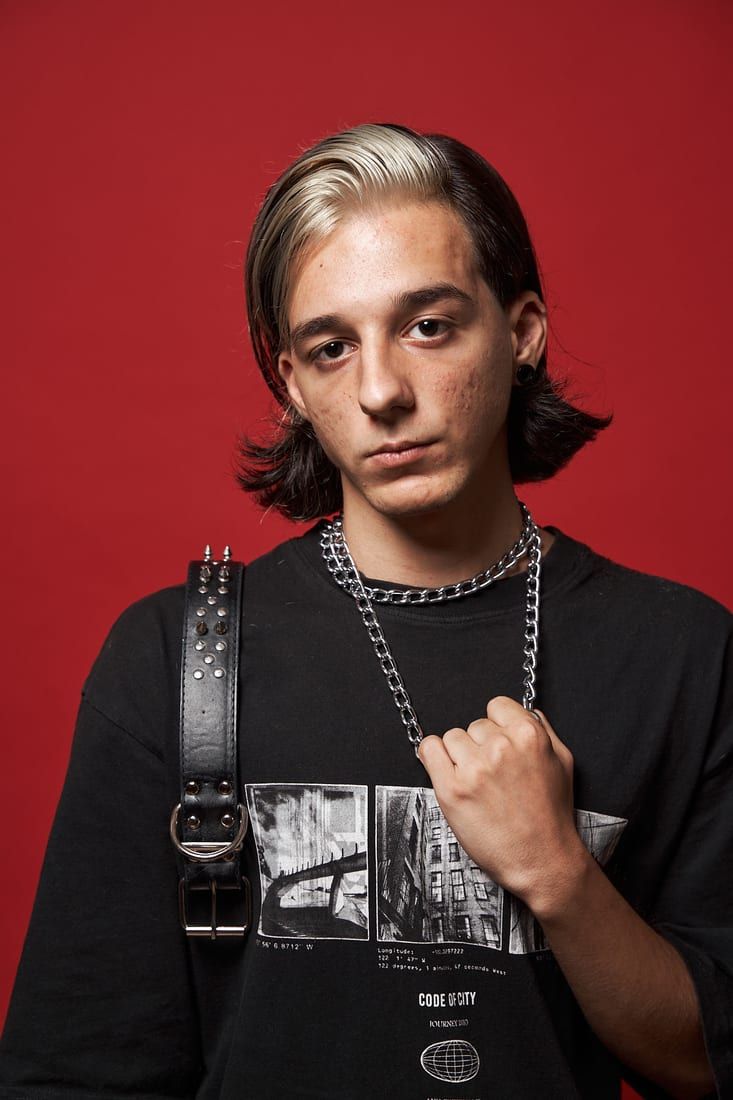 Tânăr cu tunsoare modernă și păr lung, portret pe fundal roșu